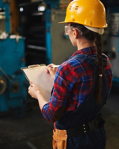 Young engineer in uniform and helmet making notes